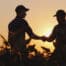 Two farmers shaking hands in the field after taking an Agris Academy Course on how to become a farmer